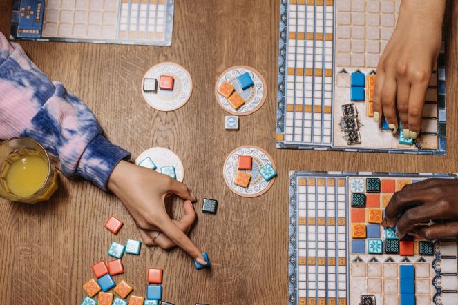 Close-up of two people's hands playing Azul, a colorful tile-based board game