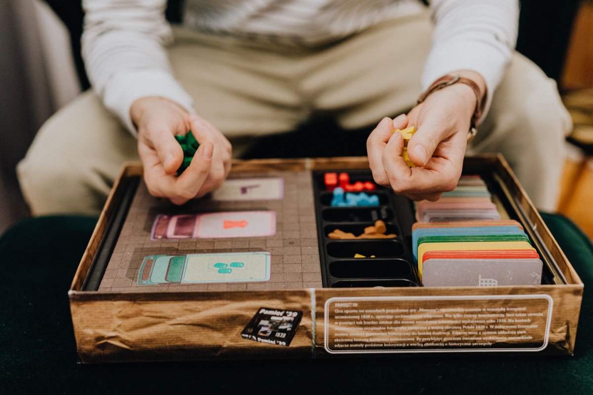 Hands lifting the tray out of a wooden box packed with colorful game components