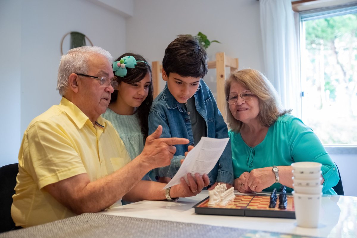 A grandparent and two children reading a game rulebook together at a table