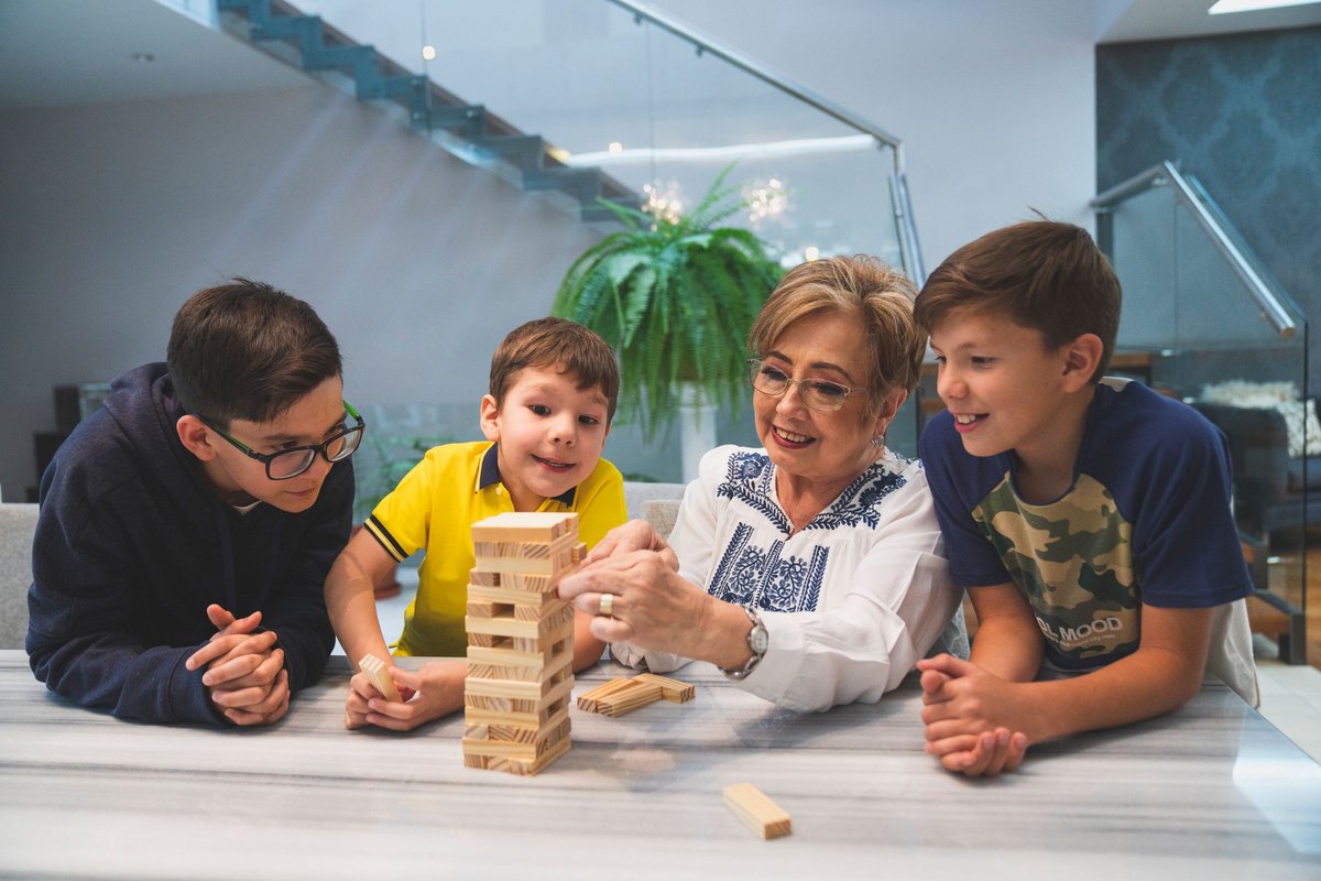 A grandmother and two boys laughing over a stacking-block game