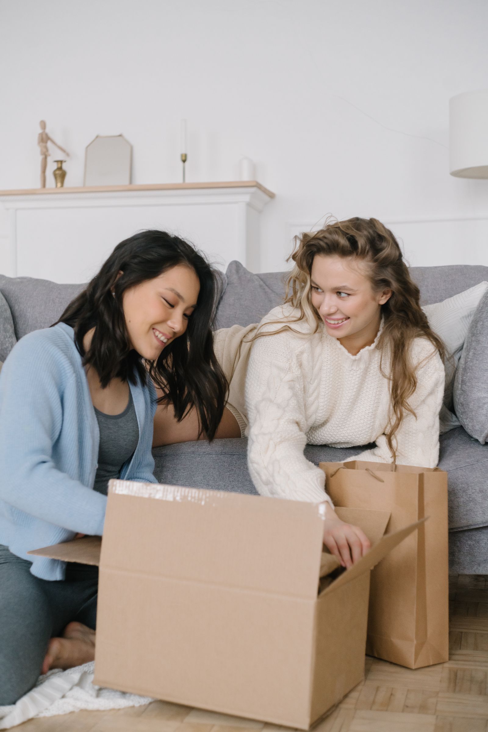 Two friends smiling while unboxing a delivery box together on a couch