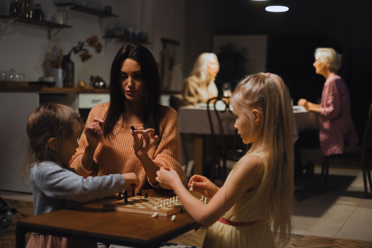 A parent and two children playing a tabletop game with grandparents nearby