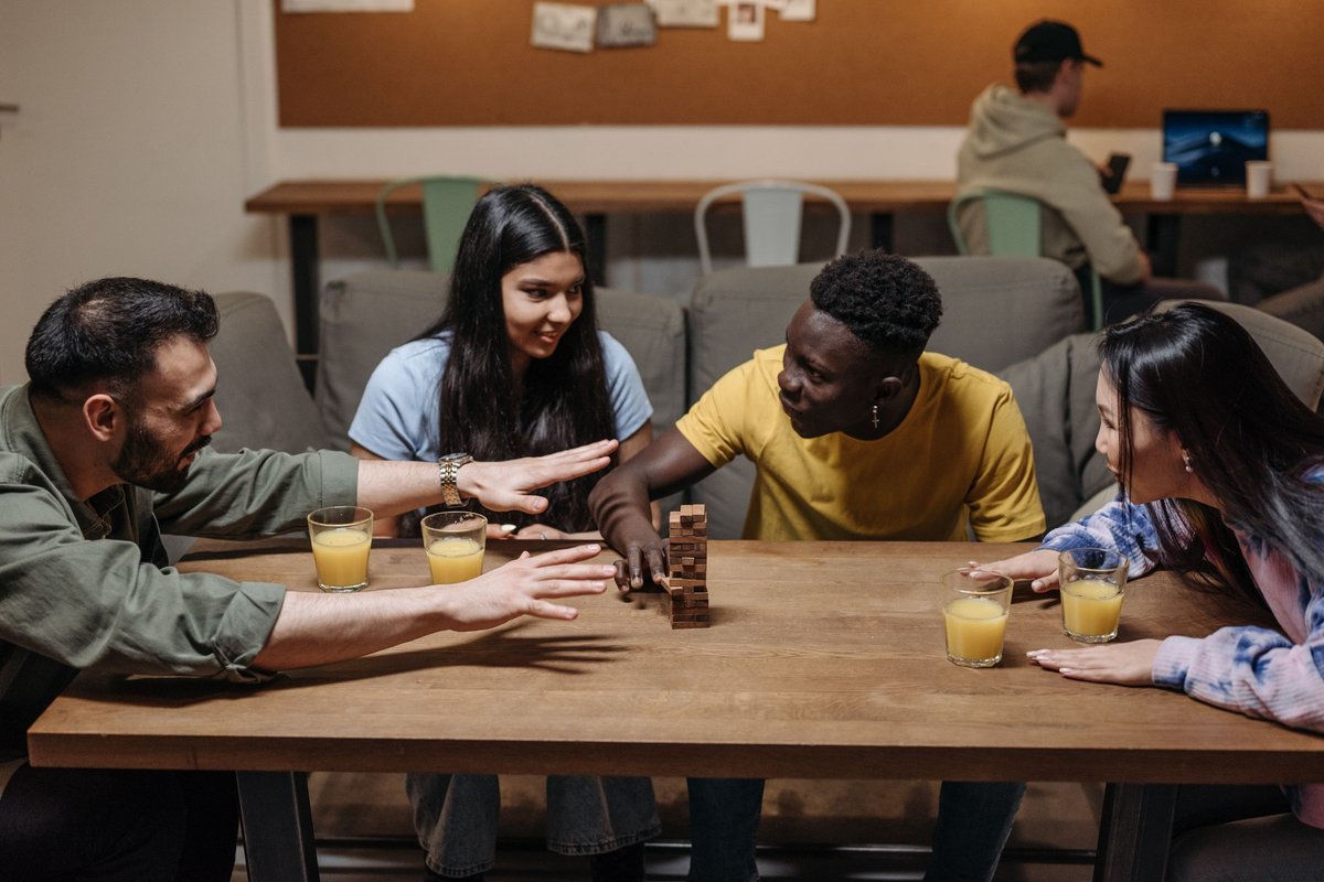 Four friends reaching across a table mid-game with drinks nearby