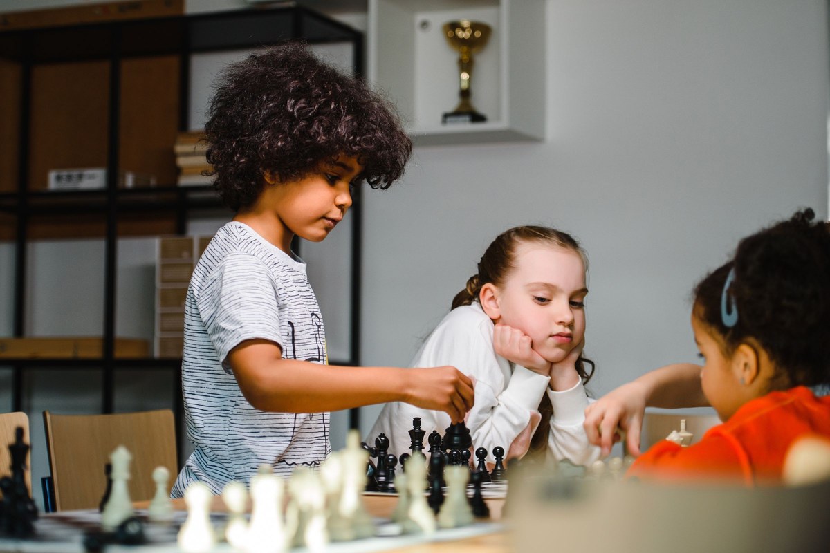 Kids leaning over a strategy board game, thinking about their next move