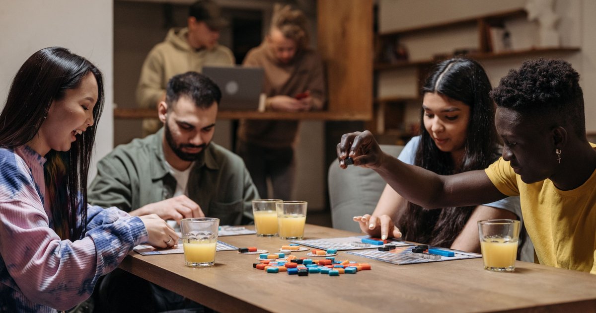 Friends gathered around a table playing a colorful board game with drinks