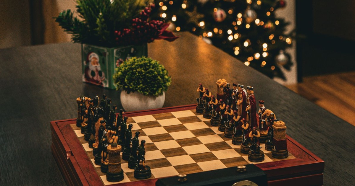 Wooden chess set on a coffee table in front of a lit Christmas tree