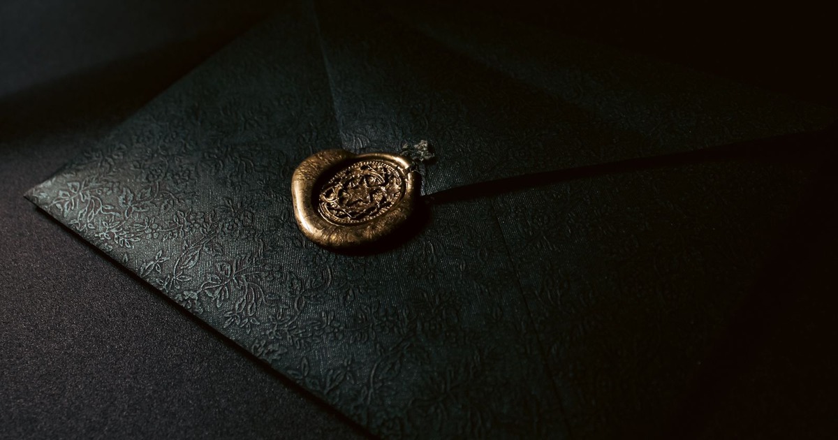 A dark green envelope sealed with a gold wax stamp