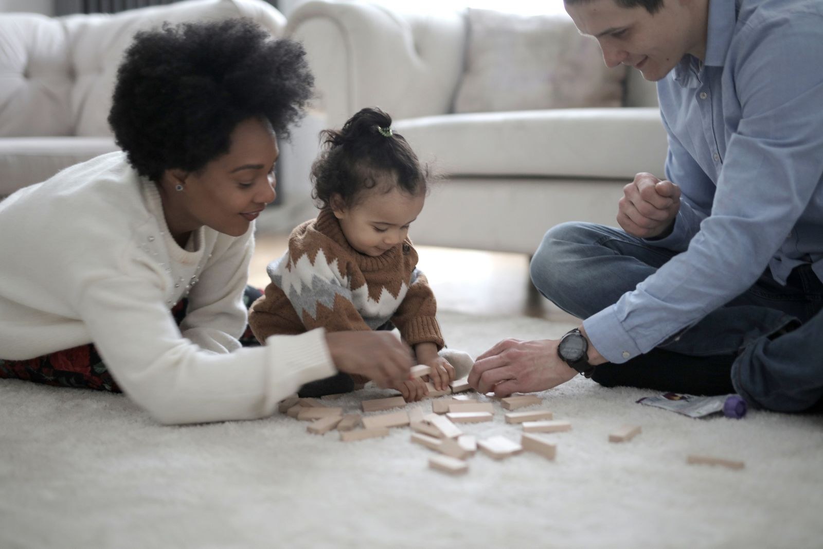 Two parents playing a wooden block game with their child on the living room floor