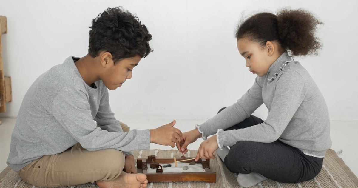 An older brother and younger sister playing a small tabletop game together on the floor