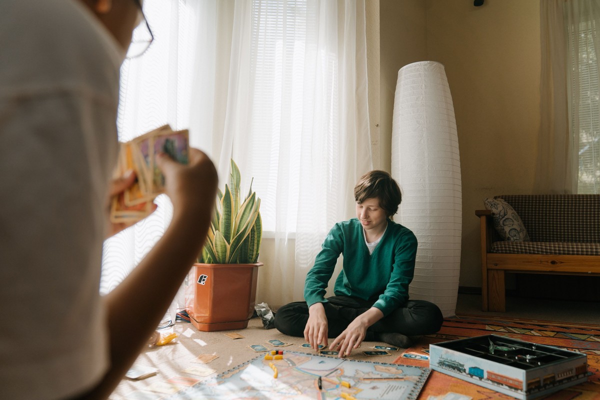 Four friends play a tile-placement game around a wooden table with glasses of orange juice