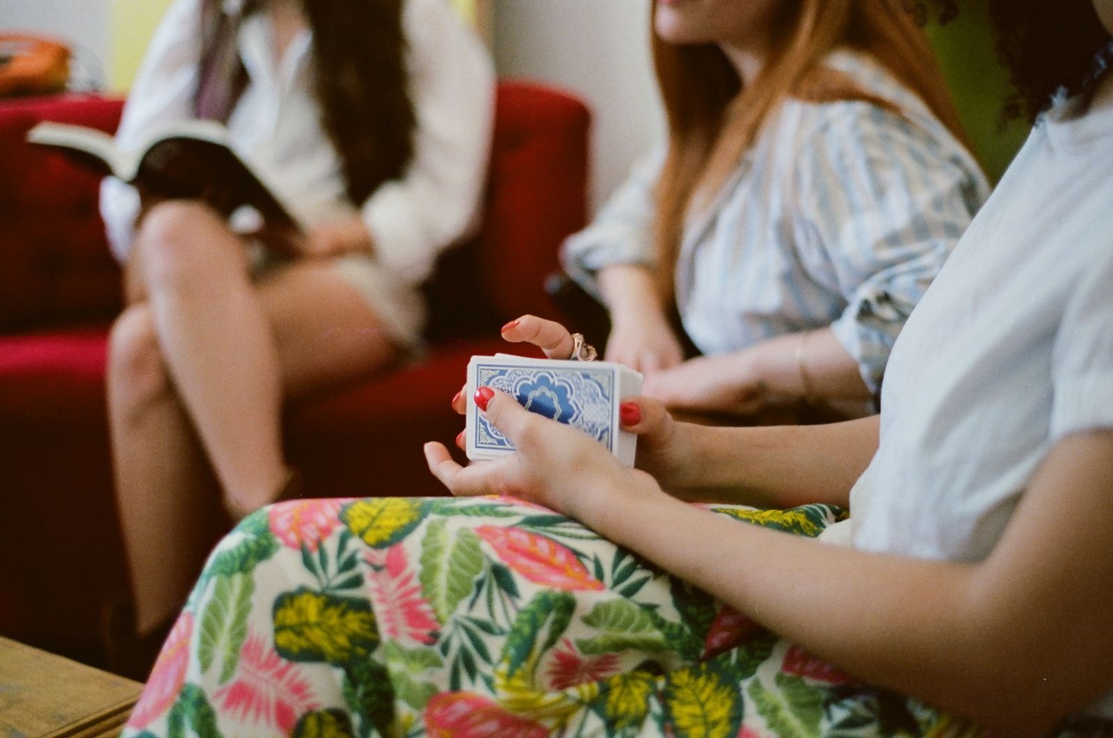 Friends on a sofa, one shuffling a deck of cards while another sits reading a book