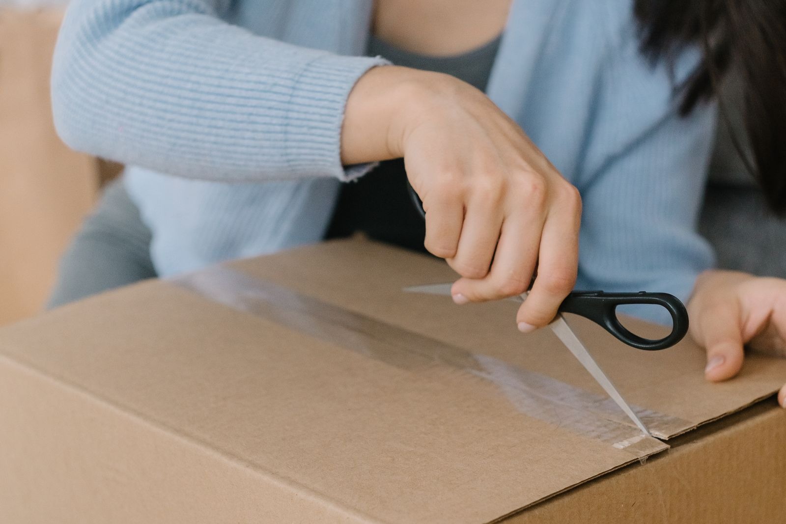 A woman cutting the tape on a plain cardboard delivery box with scissors