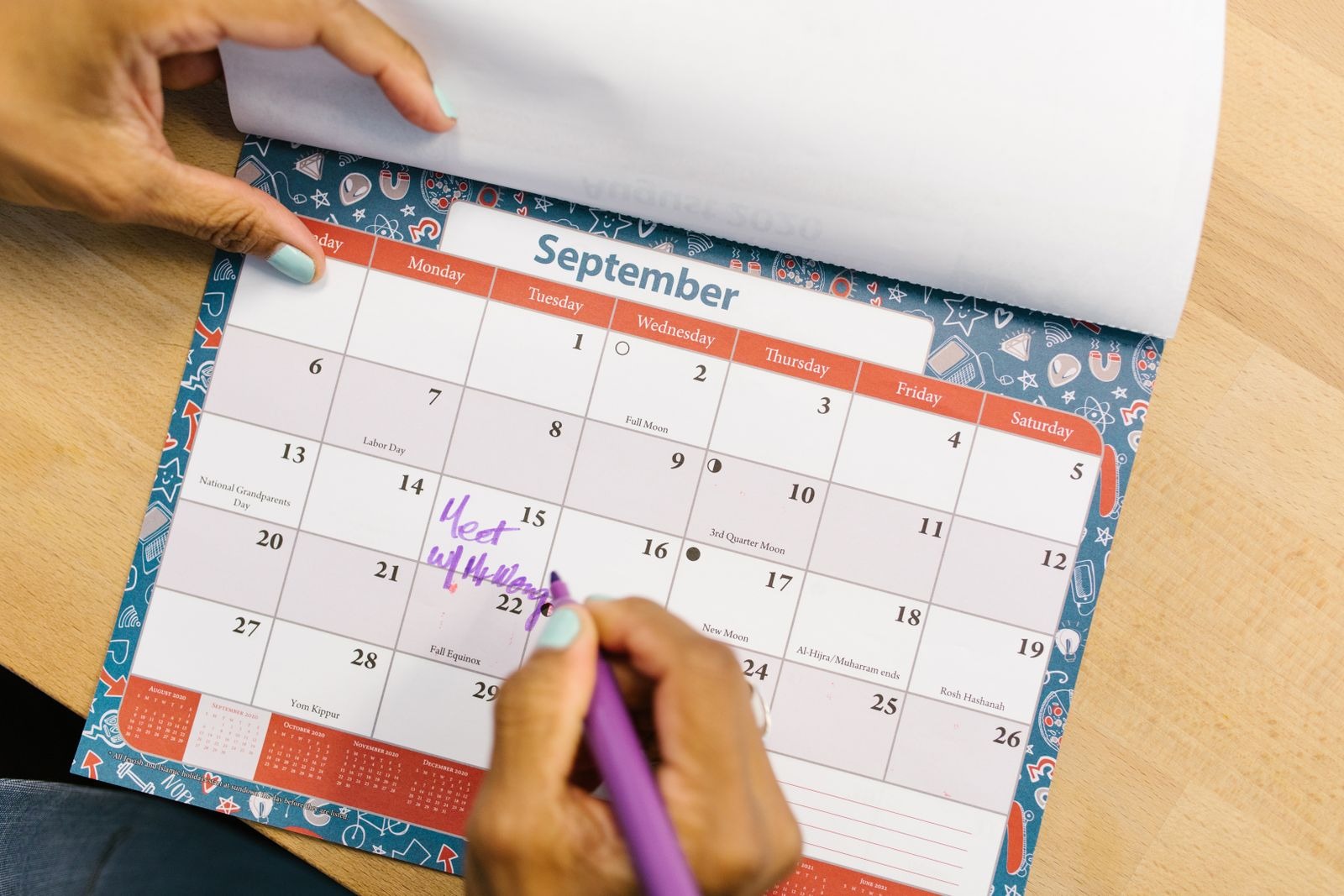 A hand writing a note on a September wall calendar with a purple marker