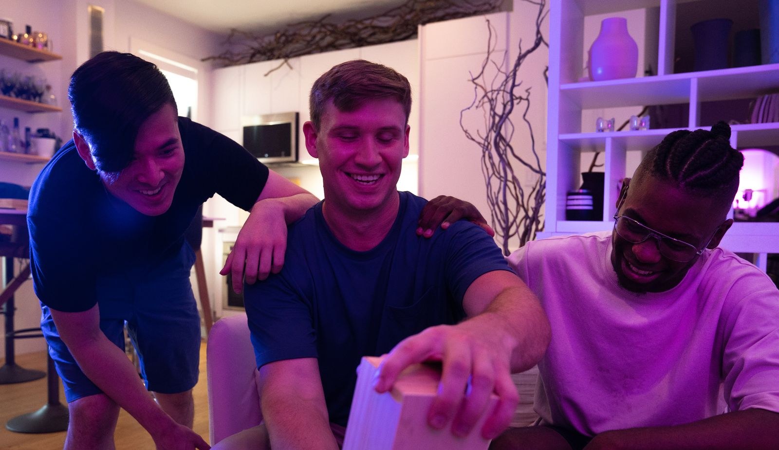 Three friends laughing as one pulls a block from a wooden tower game at a home game night