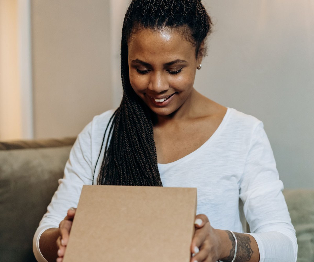 Smiling woman lifting the lid of a plain kraft box on her couch