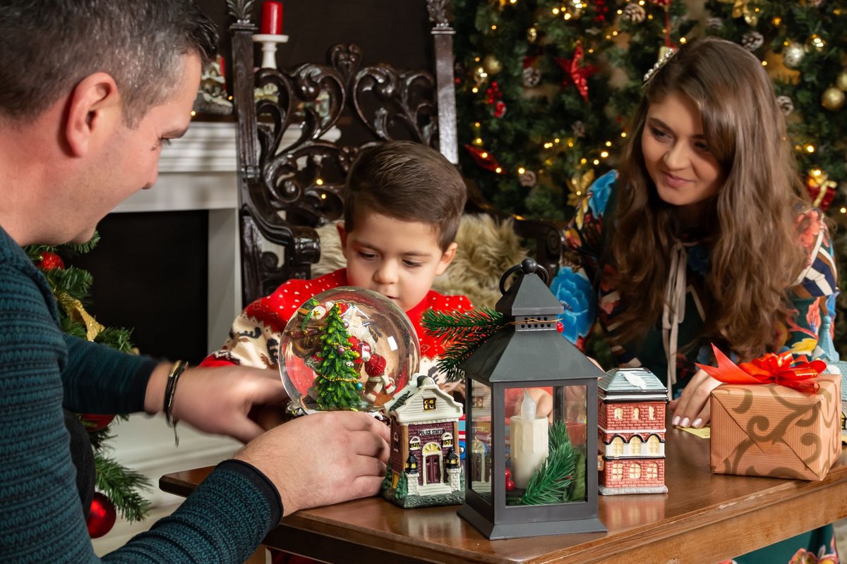 A man, woman and child at a table with a snow globe, gifts and a decorated Christmas tree behind them