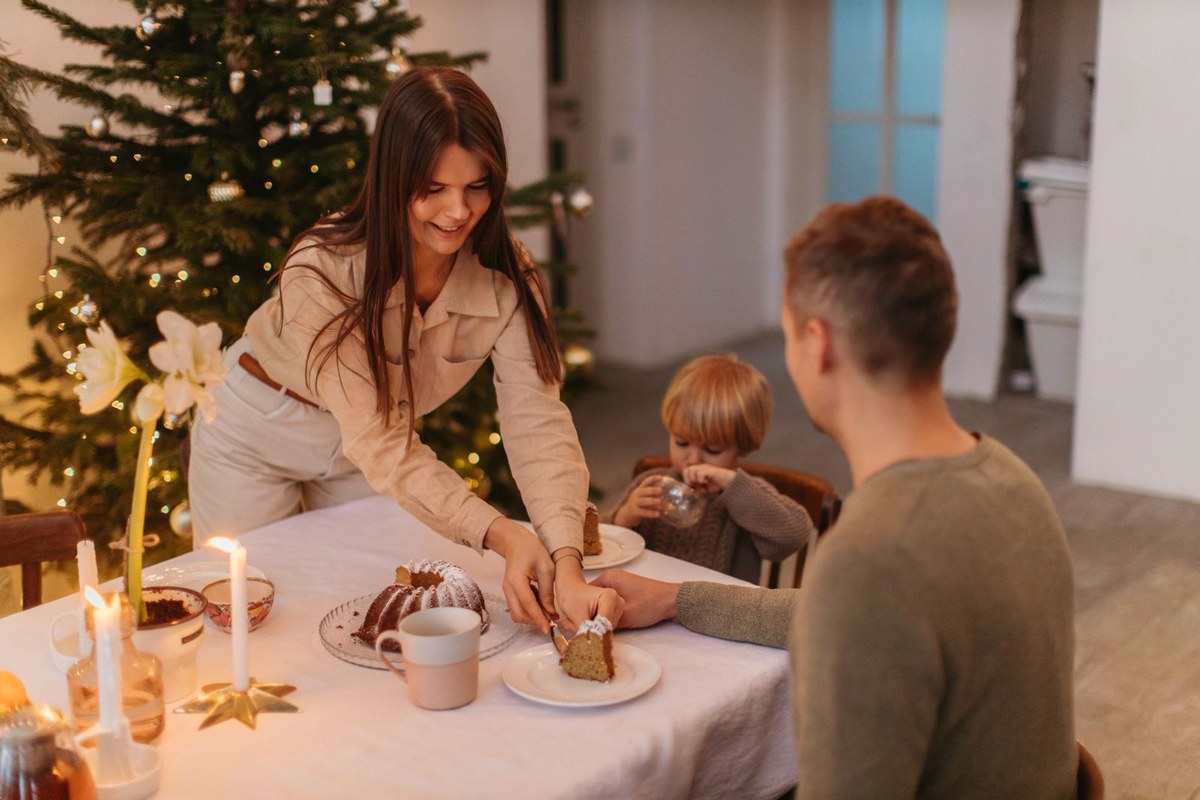 A family sharing cake at a candlelit Christmas table near a decorated tree